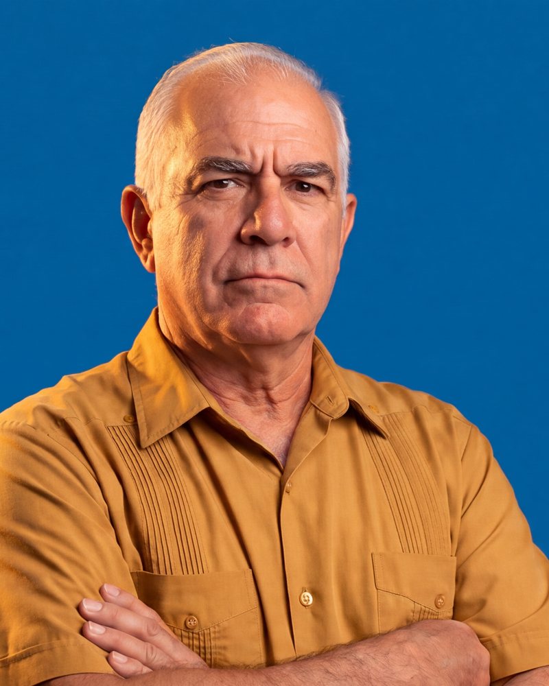 Ismael, a white-haired Cuban-American man in a mustard guayabera, arms crossed, unconvinced.