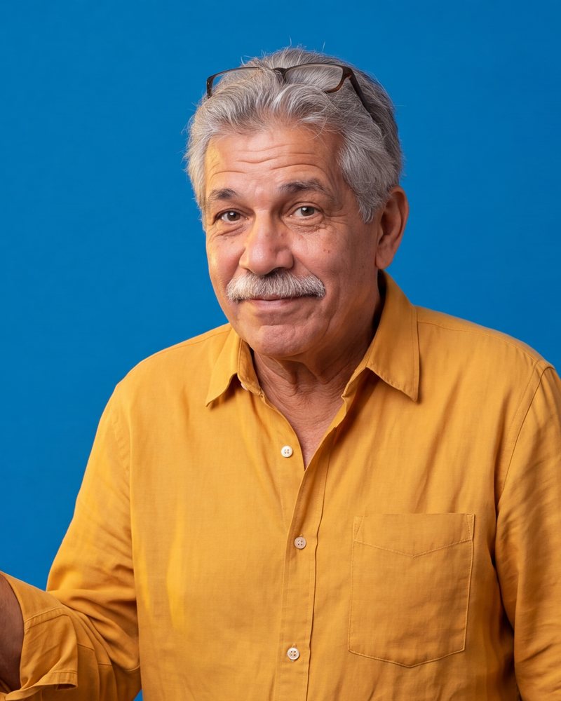Rolo, a grey-haired Cuban-American man with a moustache and glasses on his head, in a mustard shirt, half smiling.